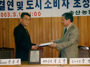 ▲ 강명규 송산면장과 제기1동의 김도원 동장이 자매결연 협정서에 서명한 뒤 서로 교환하고 있다.