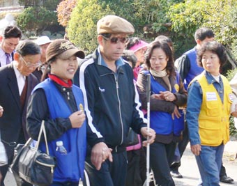 ▲ 지난 5일 걷기대회에 참가한 시각장애인과 자원봉사자들이 함께 손을 잡고 길을 걷고 있다.