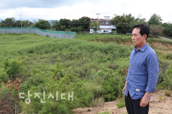 ▲ 문봉리 주민 조찬형 씨가 예산주물산업단지 부지를 안타깝게 바라보고 있다. 그의 뒤로 보이는 집이 면천면 문봉리에 속한 조 씨의 집이고, 그 앞에 2차선 도로 하나를 사이에 두고 예산주물산업단지 공사장 팬스가 쳐져 있다.