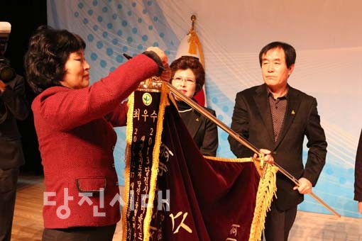 새마을지도자 대회 읍·면·동협의회 평가에서 최우수상을 수상한 당진1동협의회에 한창애 지회장(왼쪽)이 우승기를 전달하고 수치를 달고 있다.